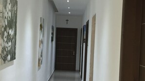 A corridor with a dark wooden door at the end, white walls, and several framed pictures on the left. - Malta Rent Rooms (Gzira)