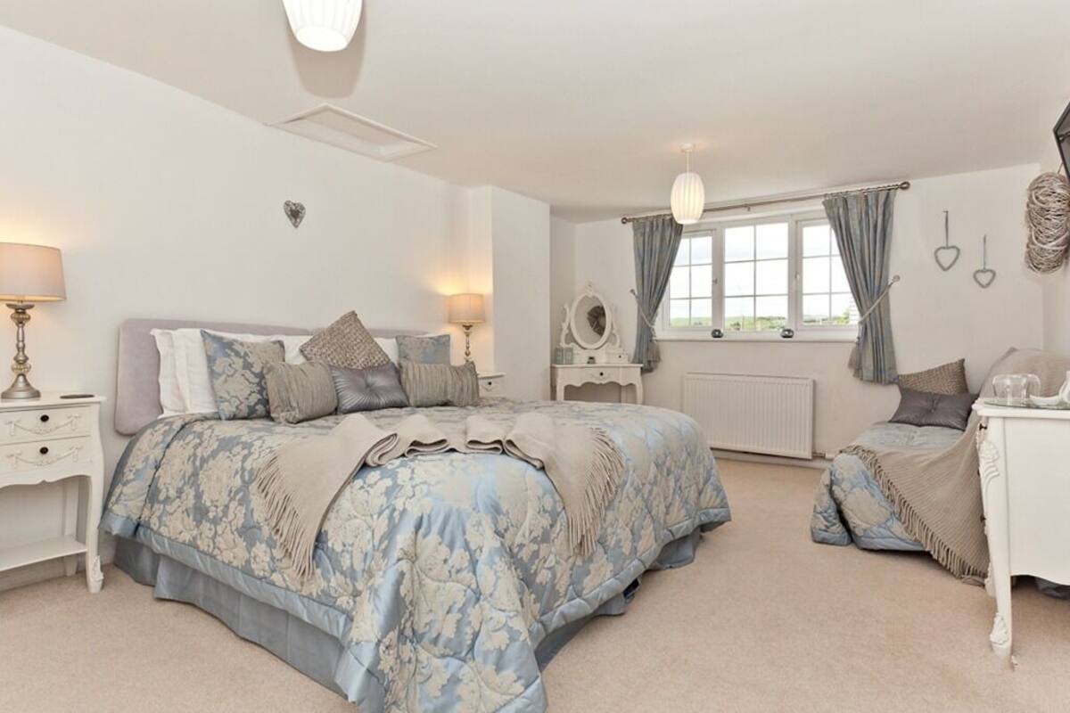 Une chambre à coucher avec un grand lit, des tables de chevet, une commode, un miroir et une fenêtre avec des rideaux.