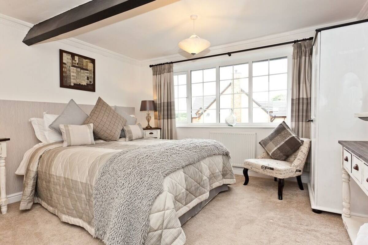 Une chambre à coucher avec un grand lit, une chaise, une commode et une fenêtre avec des rideaux.