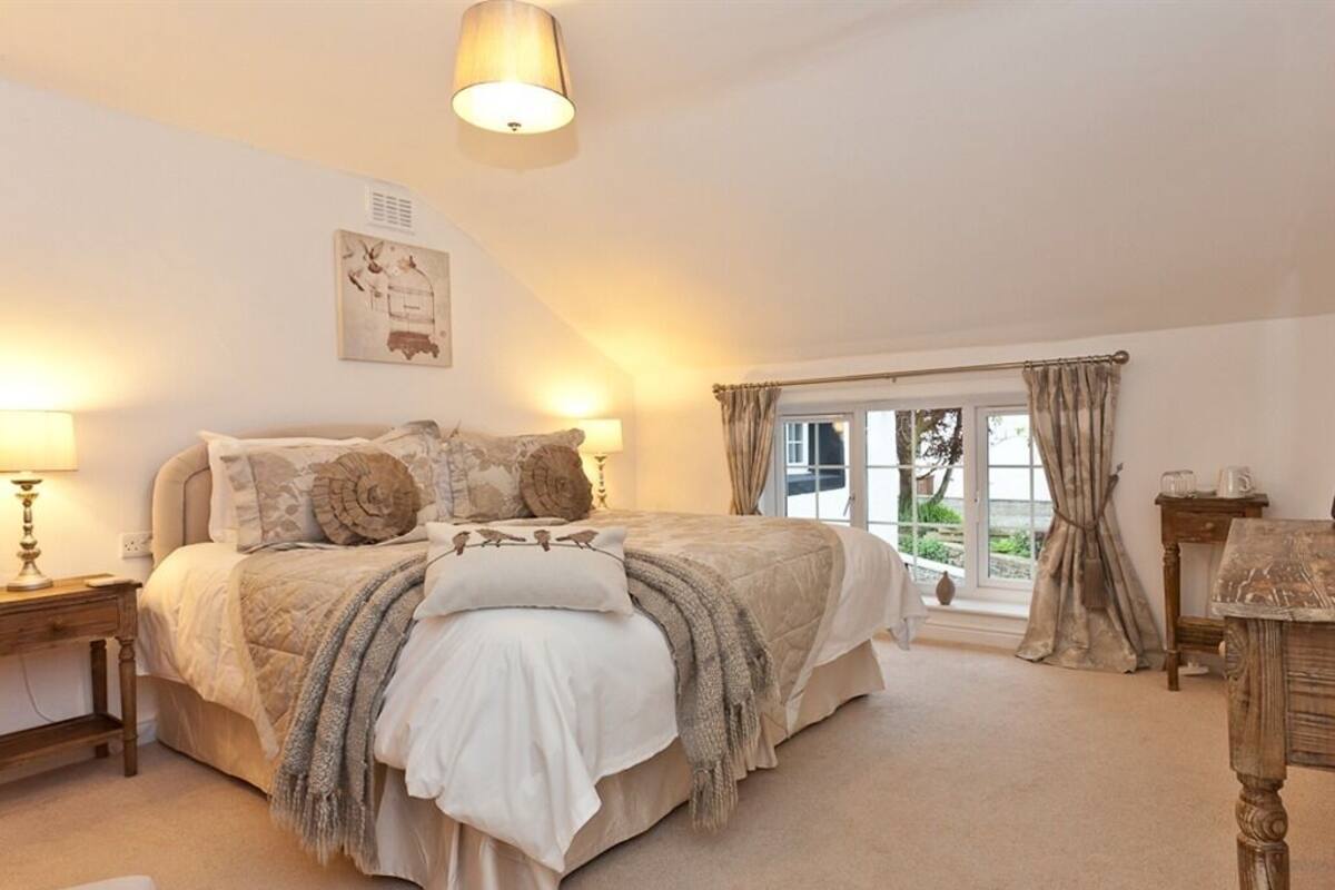Une chambre à coucher avec un grand lit, une table de chevet, une lampe, une fenêtre avec des rideaux et une vue sur l’extérieur.