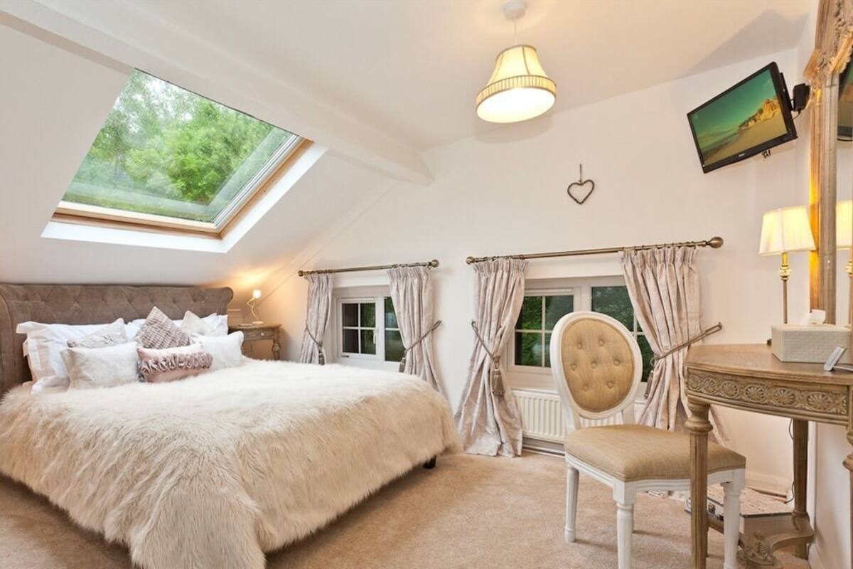 Une chambre avec un grand lit, un bureau, une chaise, une télévision et une fenêtre de toit.
