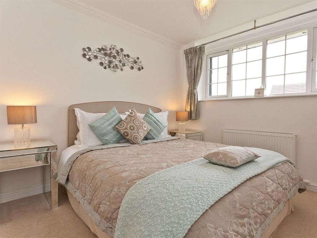 A bedroom with a large bed, two bedside tables, a wall-mounted light fixture, a window with curtains, and a radiator.