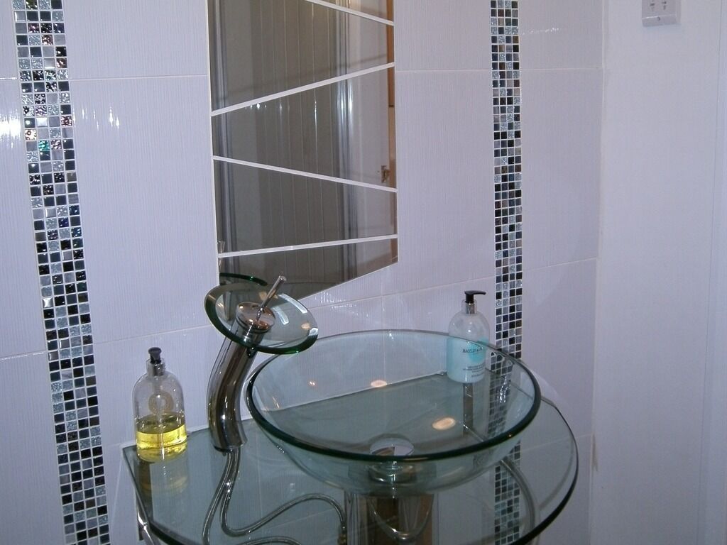 A bathroom with a glass sink, a mirror, and a shower.