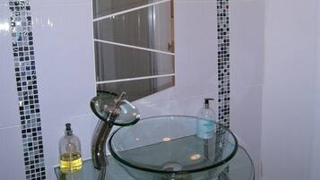 A bathroom with a glass sink, a mirror, and a shower.
