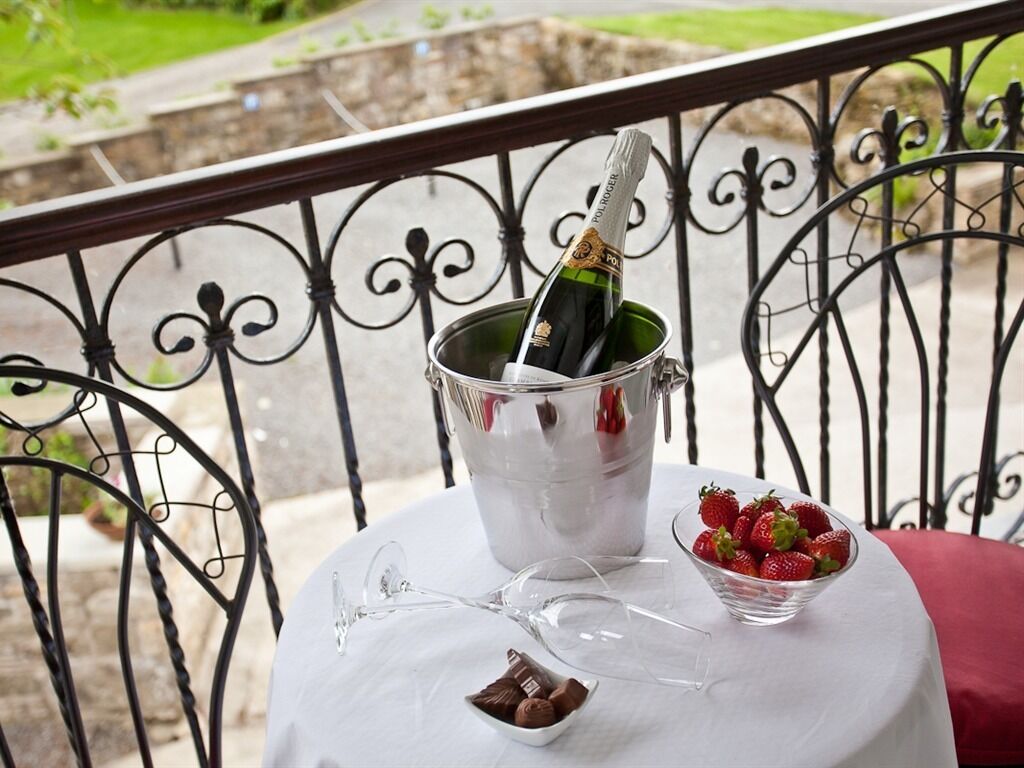 A balcony with a metal railing, a table with a bottle of champagne, a bowl of strawberries, and a glass.