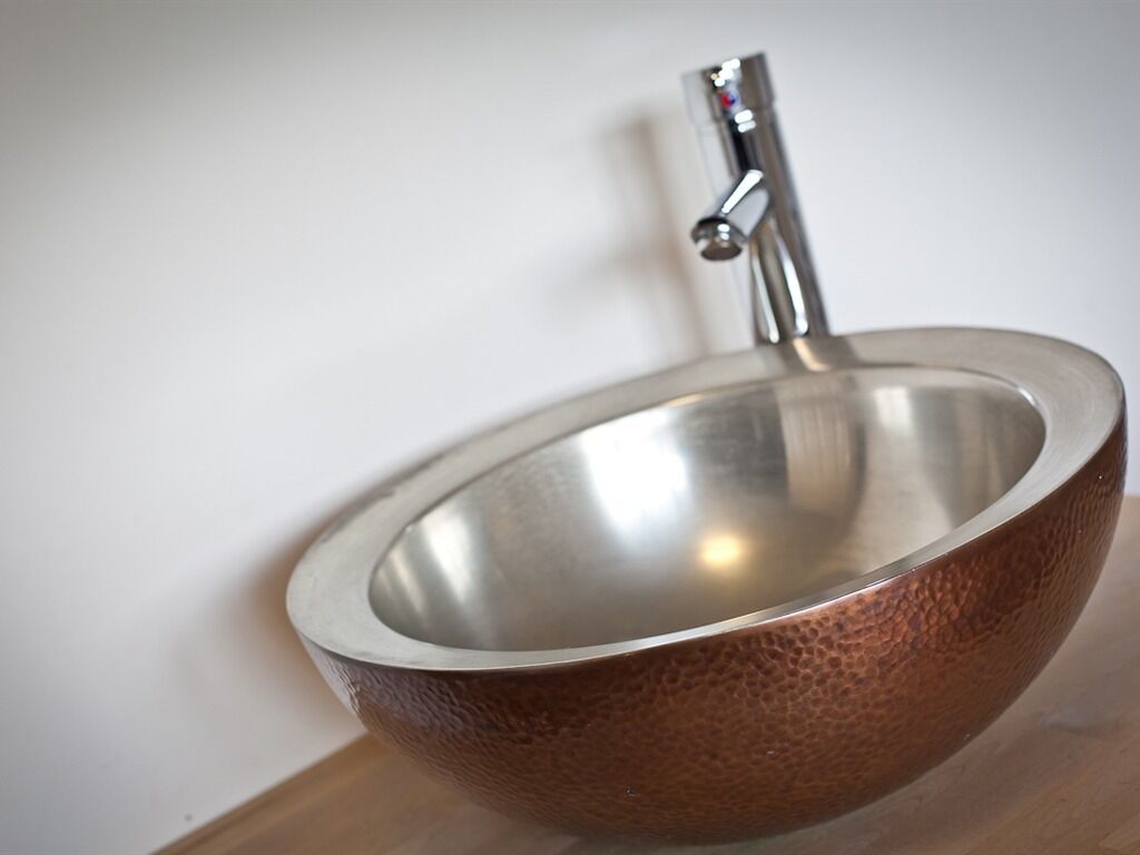 A metallic bowl sink with a faucet mounted on a wall.