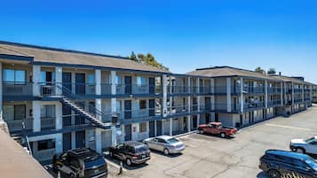A multi-story motel with balconies, a parking lot, and a clear blue sky.