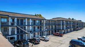 Un motel de varios pisos con balcones, un estacionamiento y un cielo azul despejado.