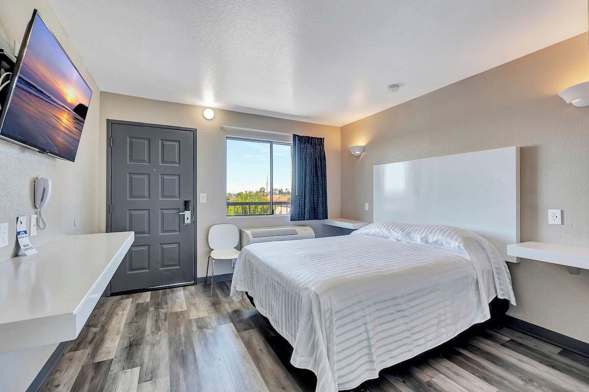 A hotel room with a bed, a desk, a chair, a TV, and a window with a view.