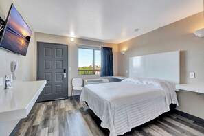 A hotel room with a bed, a desk, a chair, a TV, and a window with a view.