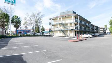 Um motel com placa indicando tarifas econômicas, um edifício de vários andares, estacionamento e alguns carros estacionados.