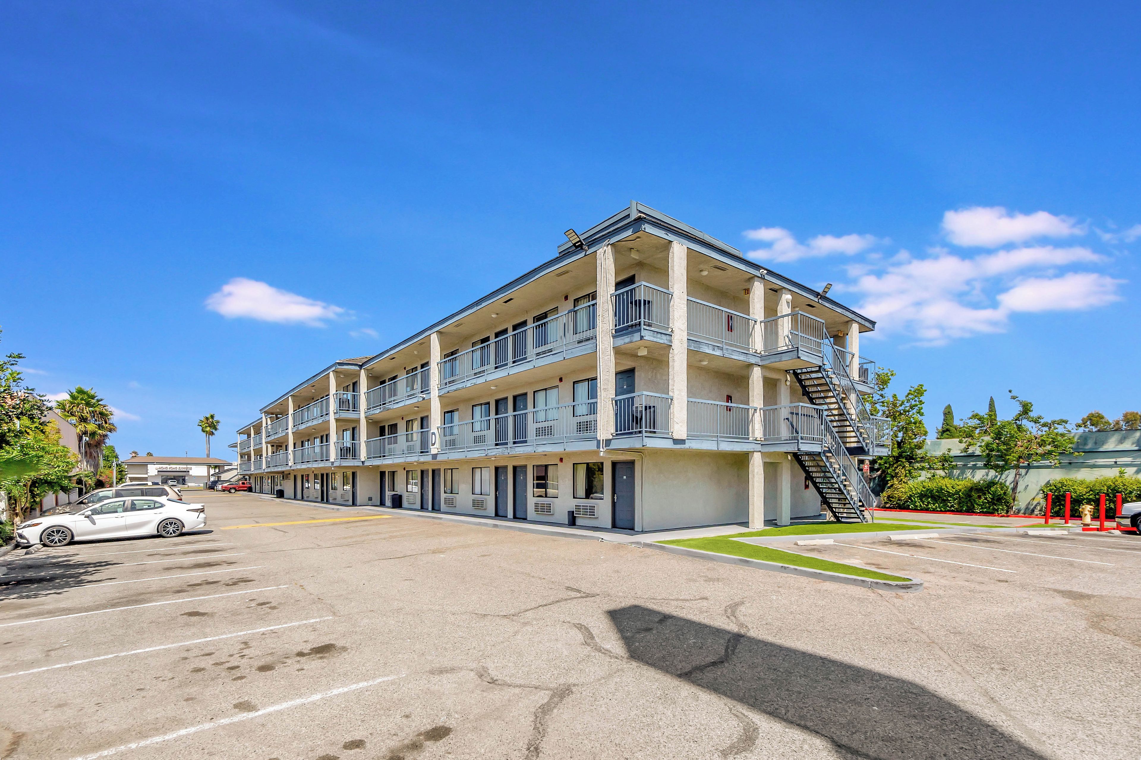 Un motel à plusieurs étages avec un parking, une borne d’incendie et un palmier.