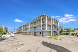 Un motel de varios pisos con estacionamiento, un hidrante y una palmera.