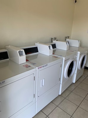 A laundry facility with multiple washing machines and dryers, including a front-loading washer and a top-loading dryer. - Morada Inn - Near Garden Grove Park (Garden Grove)