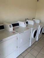 Uma lavanderia com várias máquinas de lavar e secar, incluindo uma máquina de lavar frontal e um secador de abertura superior.