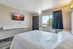 Una habitación de hotel con una cama, un televisor montado en la pared, una ventana con cortinas y una puerta.
