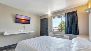 Una habitación de hotel con una cama, un televisor montado en la pared, una ventana con cortinas y una puerta.