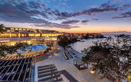 A resort with multiple buildings, a beach area with sun loungers, and a view of the sea.