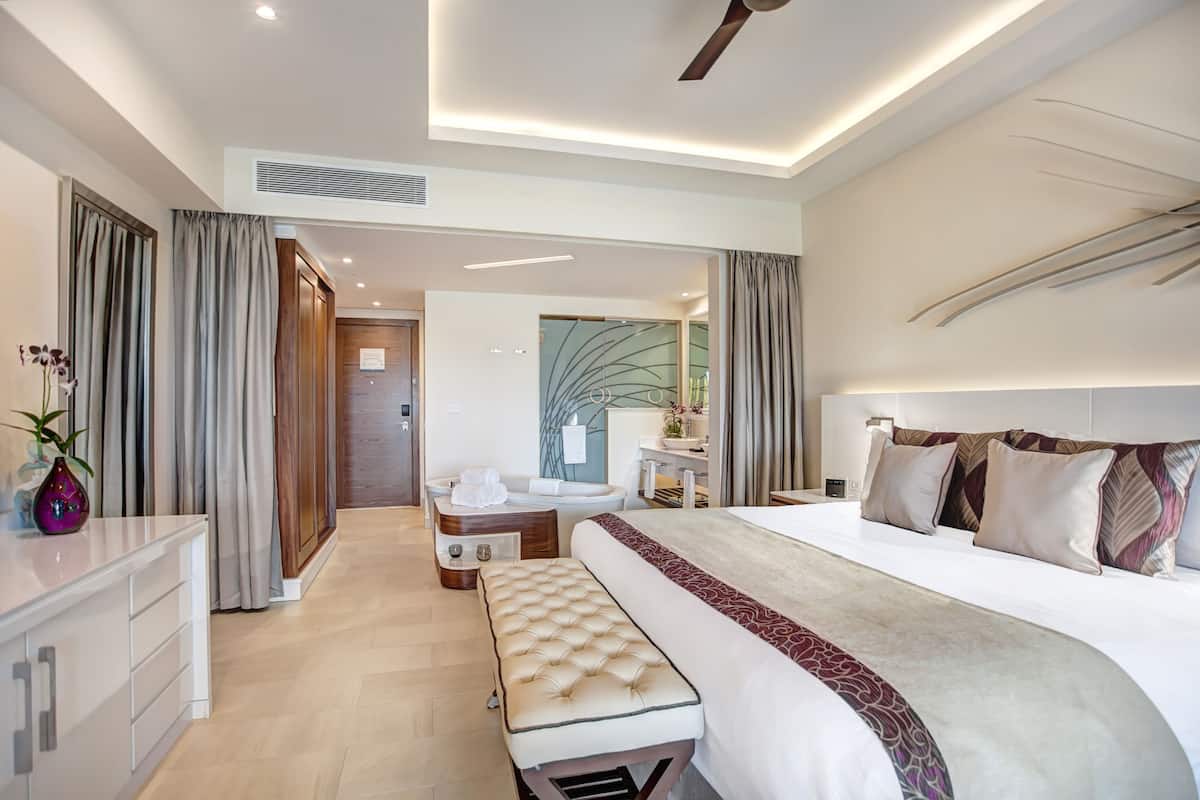 Ein modernes Hotelzimmer mit einem großen Bett, einem Schminktischchen, einer Bank und einem Schreibtisch.