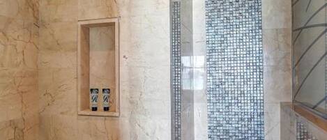 A bathroom with a shower, marble walls, and a tiled shower area.
