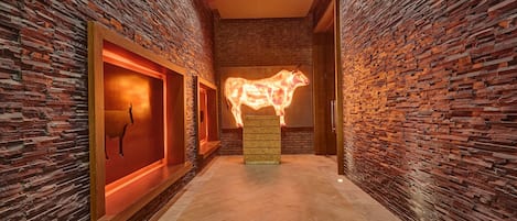 A hallway with brick walls, a central illuminated sculpture, and a wooden bench.