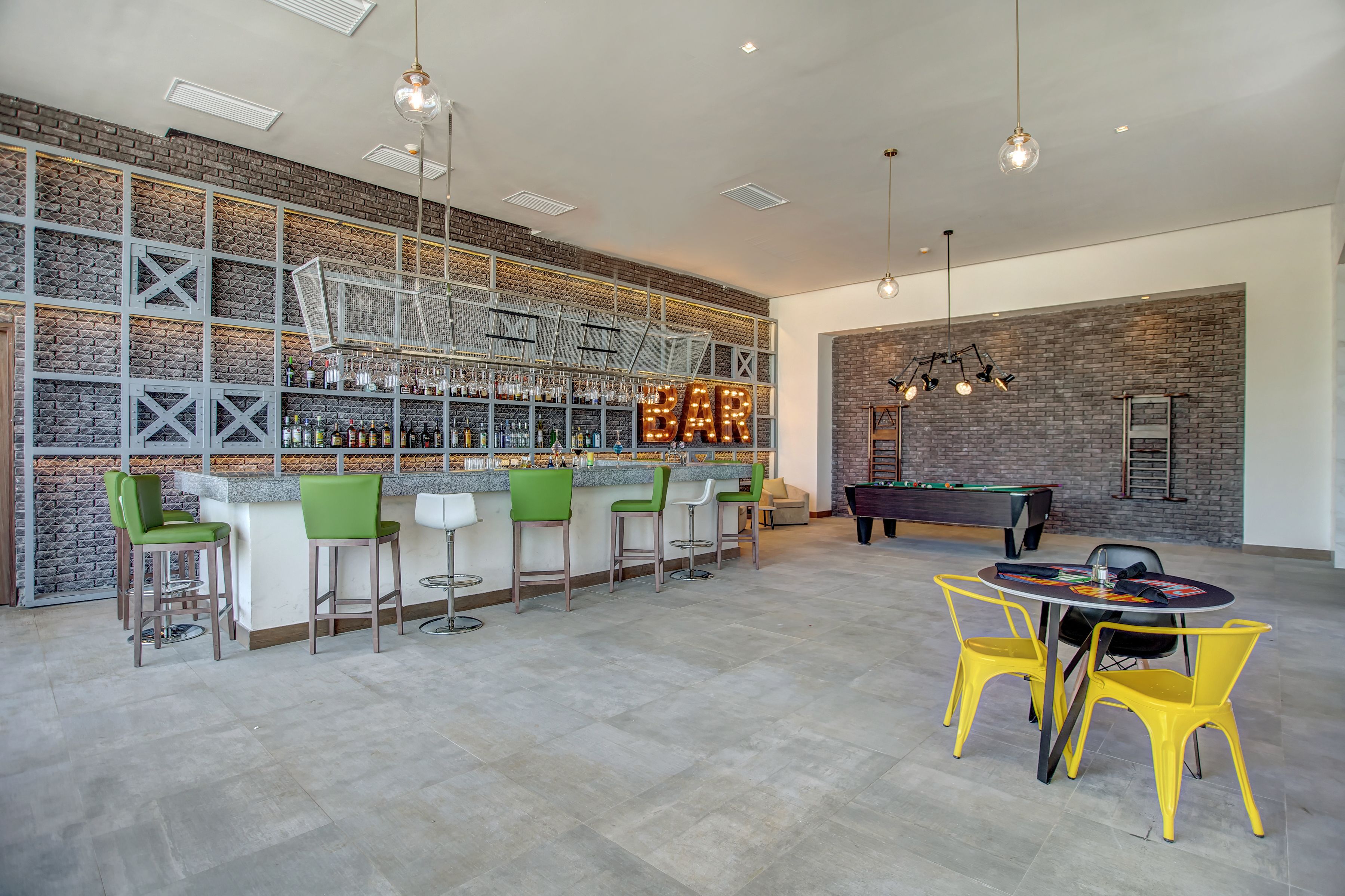 A bar area with a brick wall, green and white bar stools, and a pool table.