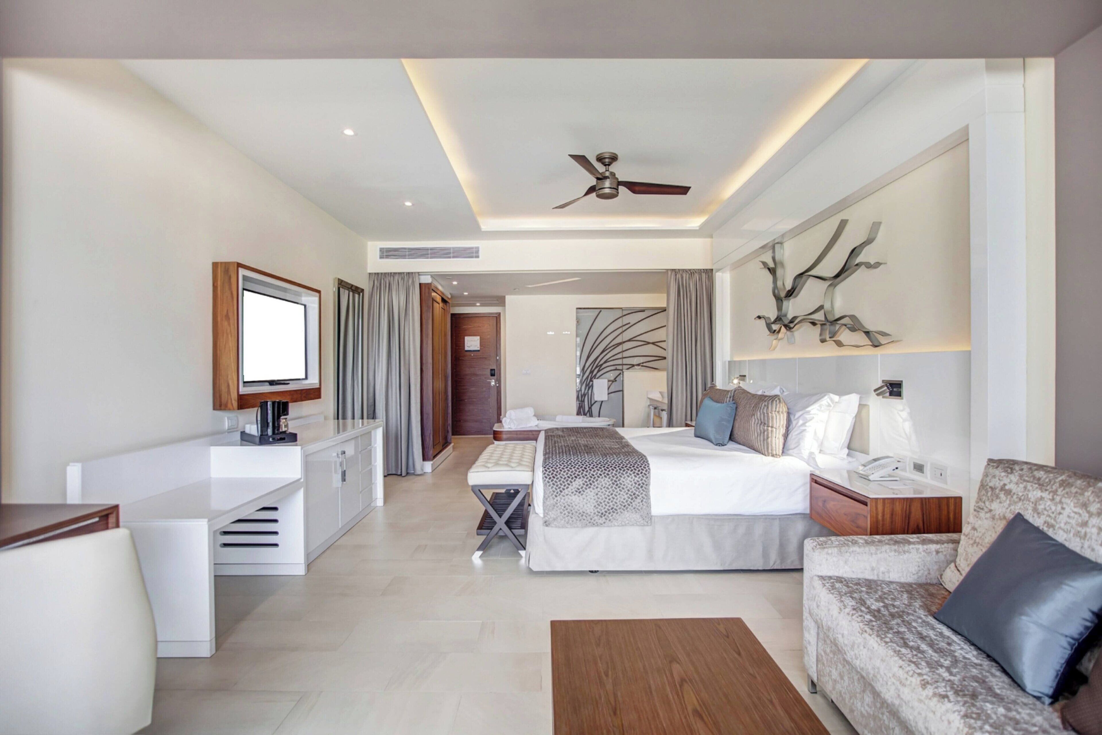 A modern hotel room with a bed, a sofa, a desk, and a television.