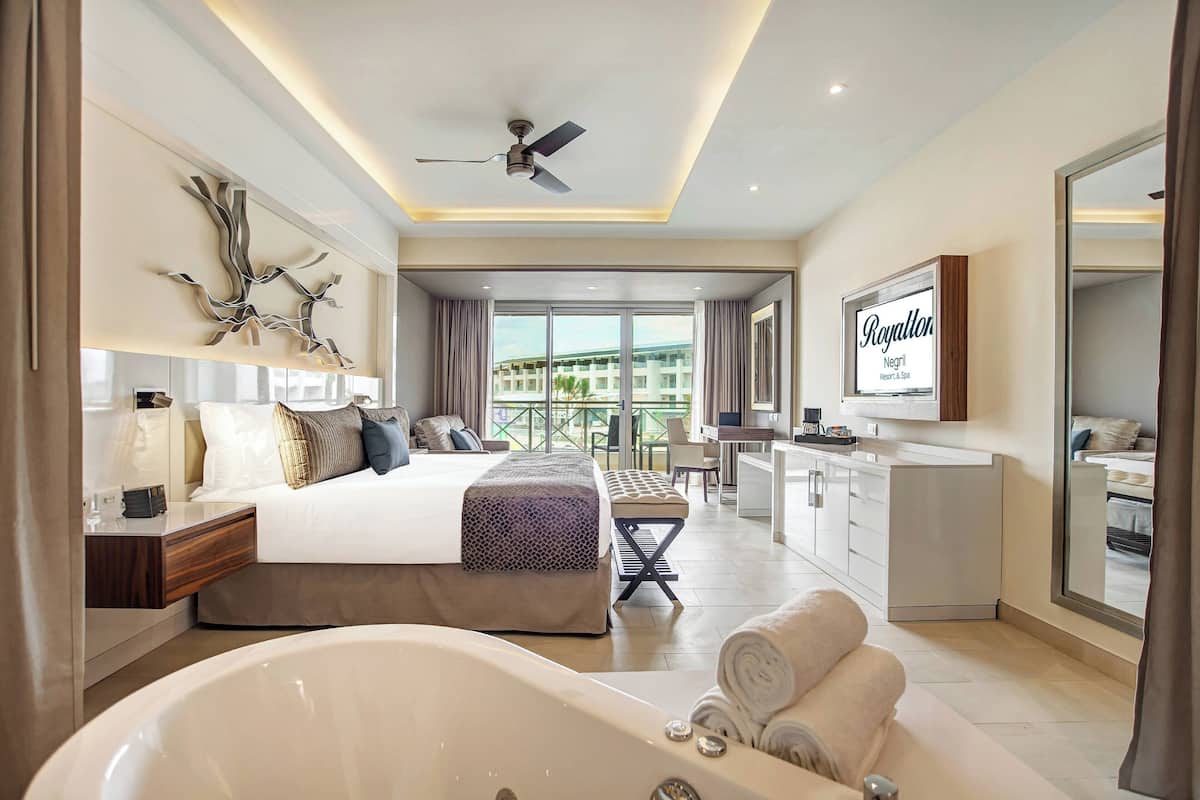 Ein modernes Hotelzimmer mit einem großen Bett, einer Sitzecke, einem Balkon und einem Badezimmer mit einer Badewanne.
