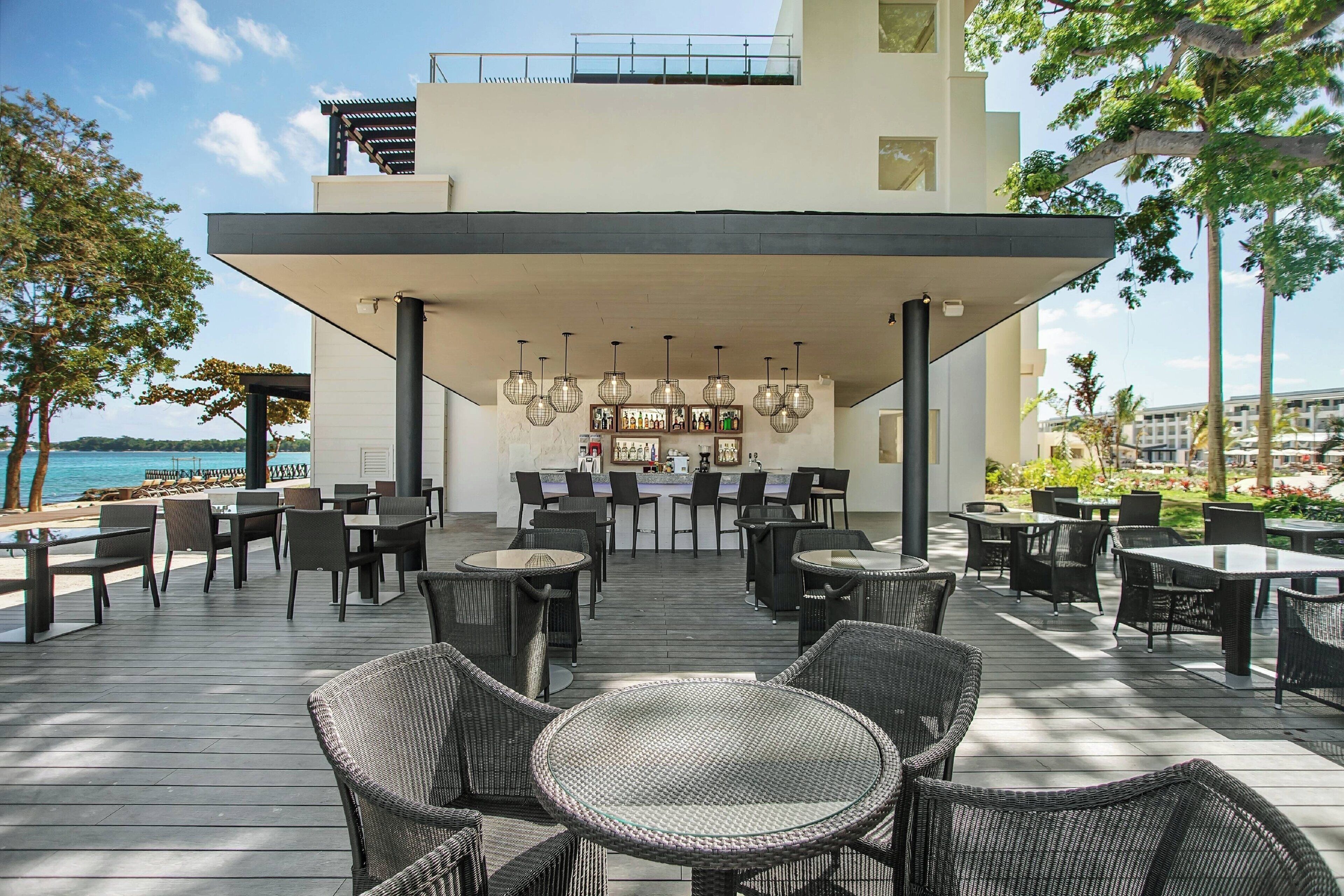 Un patio al aire libre con mobiliario de mimbre, una zona de bar y vistas al mar.