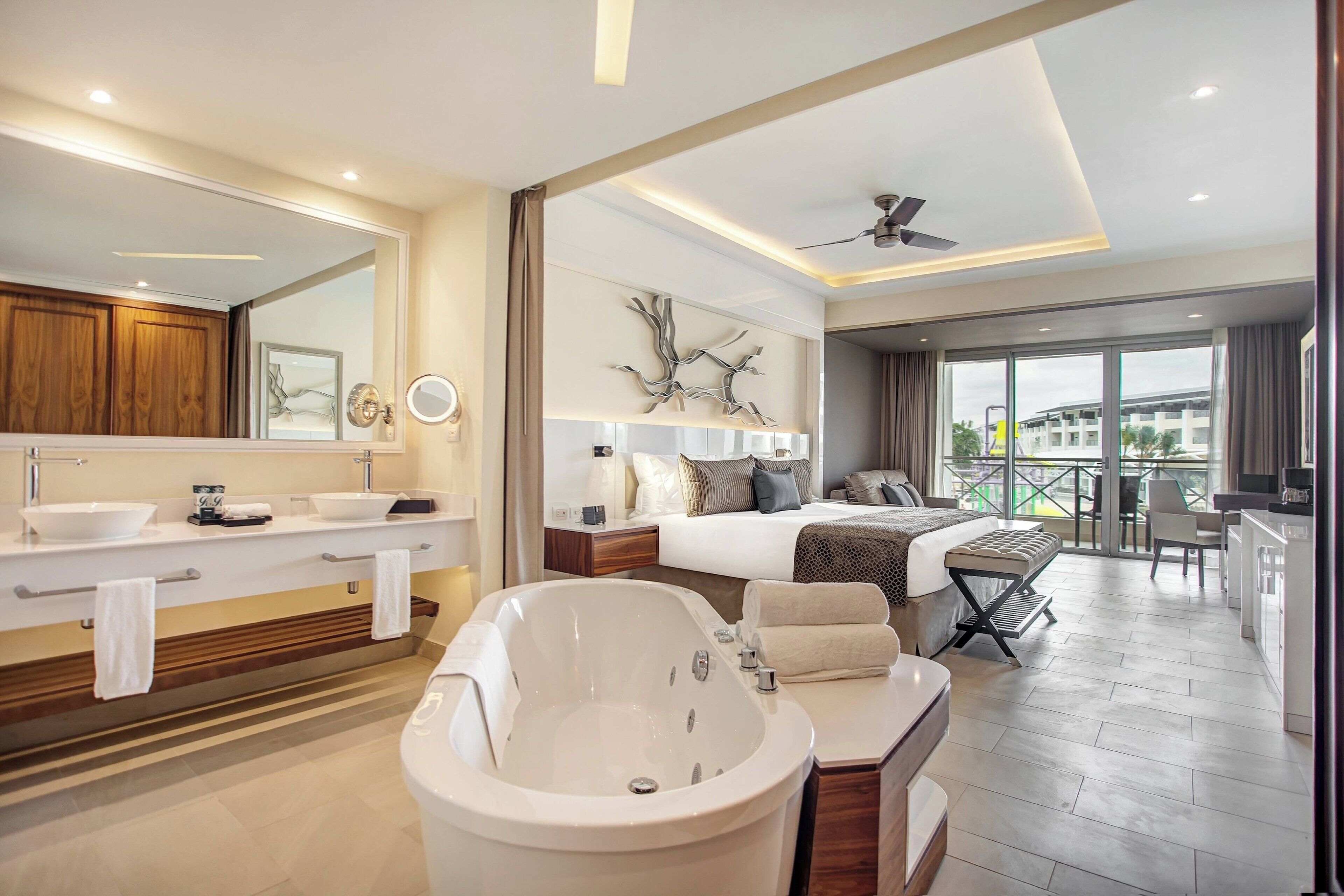 Ein modernes Hotelzimmer mit einer großzügigen Badewanne, einem Doppelbett, einem Schreibtisch und einem Balkon mit Blick.