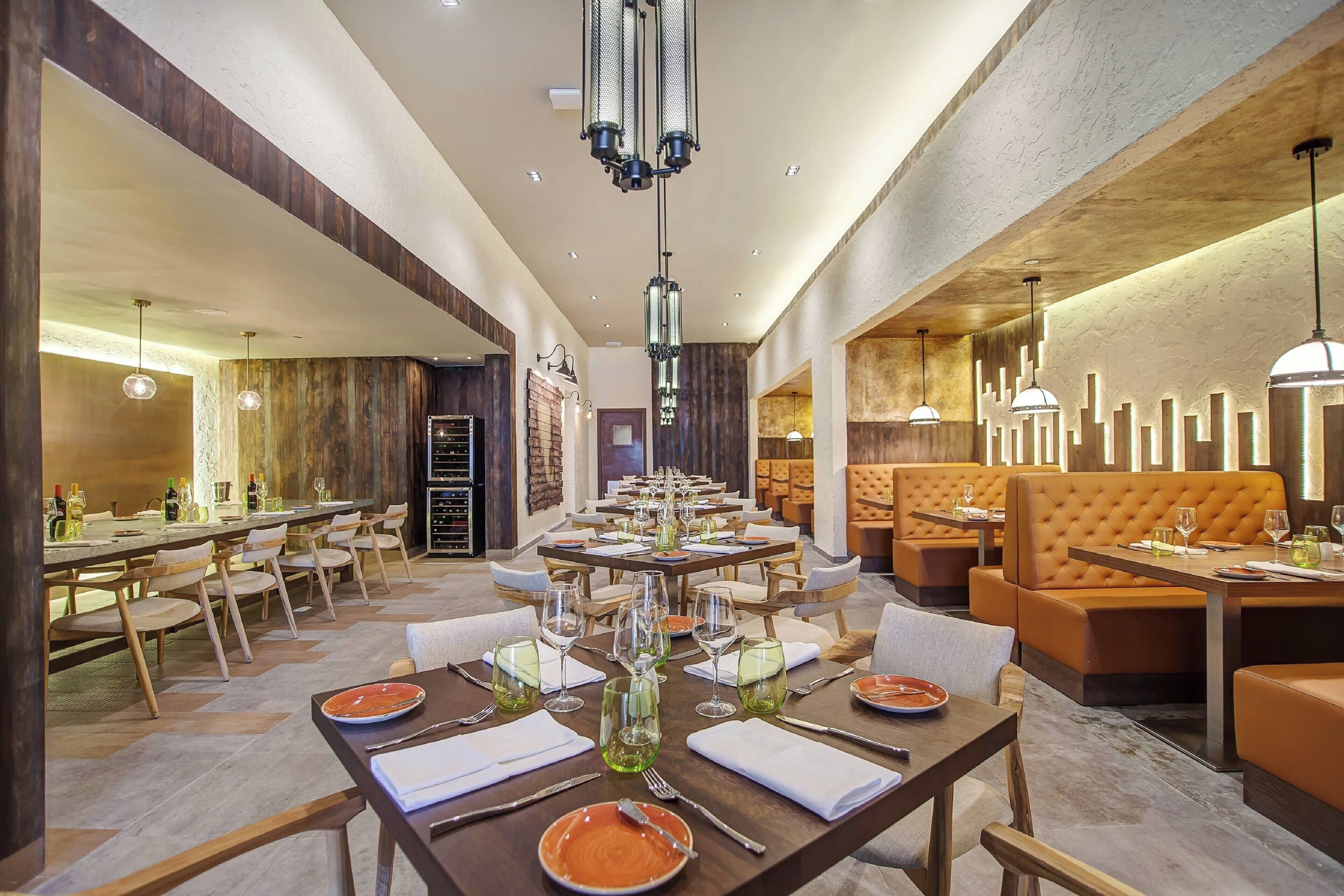 A spacious dining area with multiple tables set for guests, featuring a mix of seating arrangements and a modern chandelier.