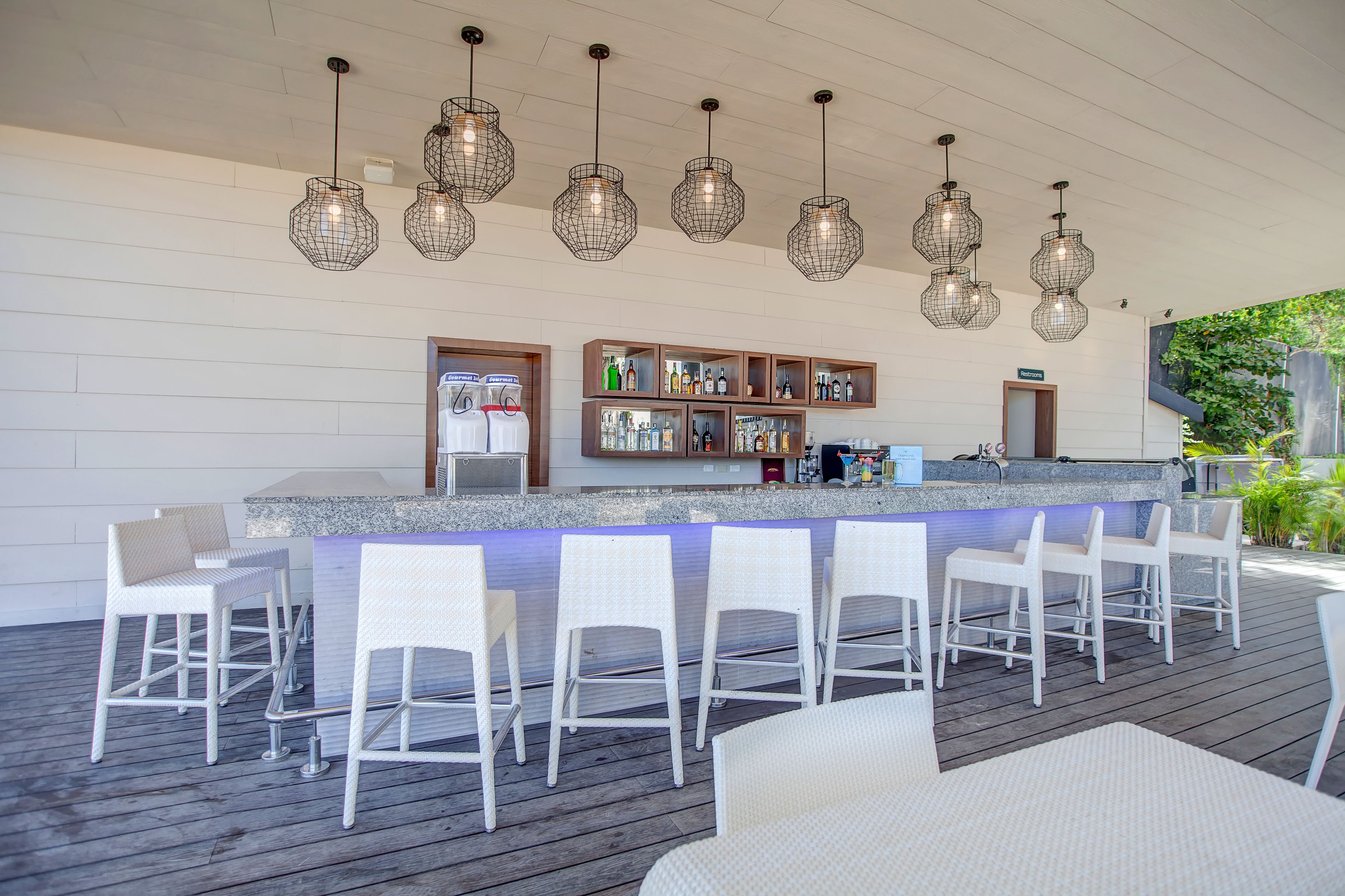 A bar area with white bar stools, a counter with bottles, and hanging wire light fixtures.