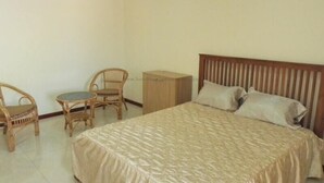 Une chambre à coucher comprenant un lit, deux fauteuils en osier, une petite table ronde et une armoire en bois.