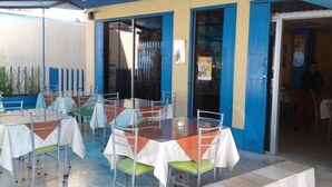 Un espacio al aire libre con mesas y sillas, una puerta azul y una entrada de vidrio.
