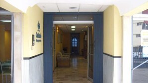 Entrada de hotel con mostrador de recepción, un área de espera con sofá y una puerta visible que da al interior.