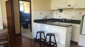 Una cocina con armarios blancos, encimera negra y dos taburetes.