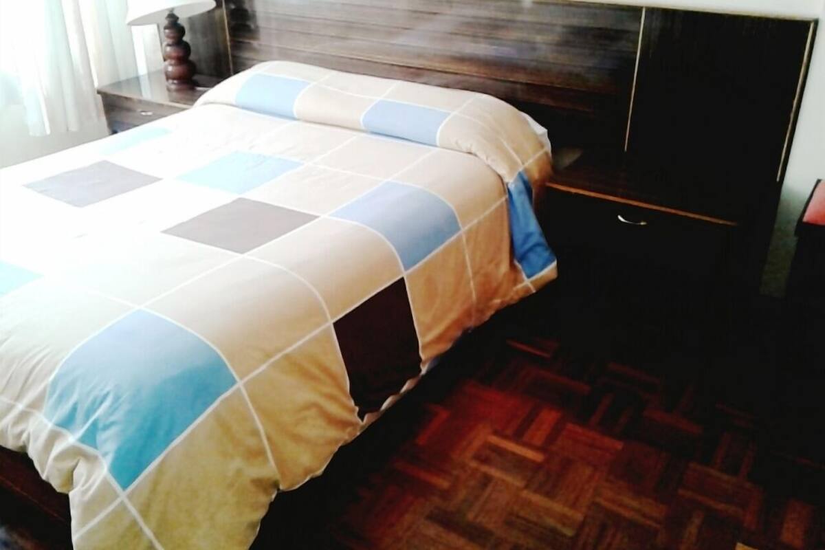 Ein Bett mit karierter Bettdecke, einem Holz-Kopfteil und einem Nachttisch mit Lampe.