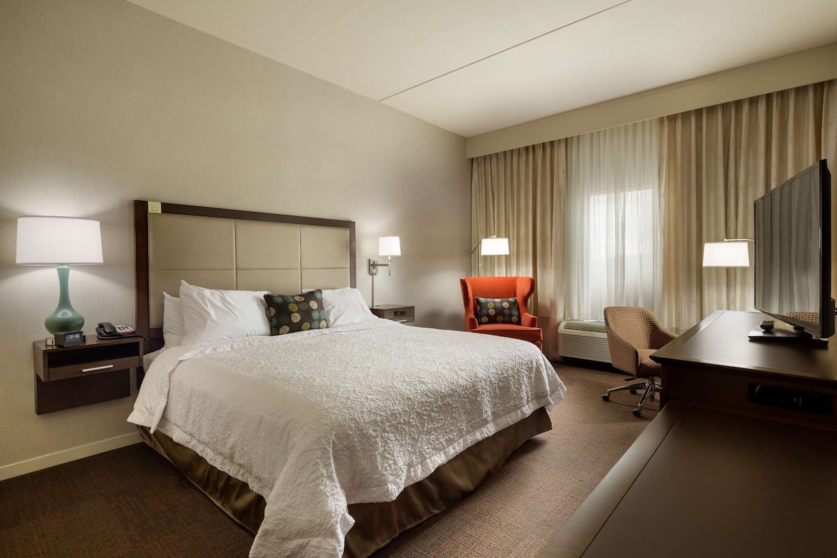 A hotel room with a large bed, a desk, a chair, and a television.
