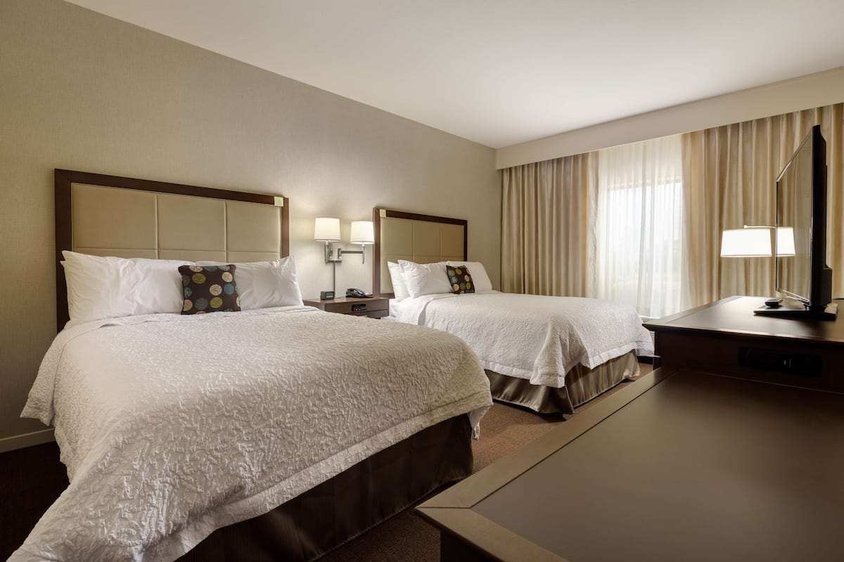 A hotel room with two beds, a desk, and a TV.