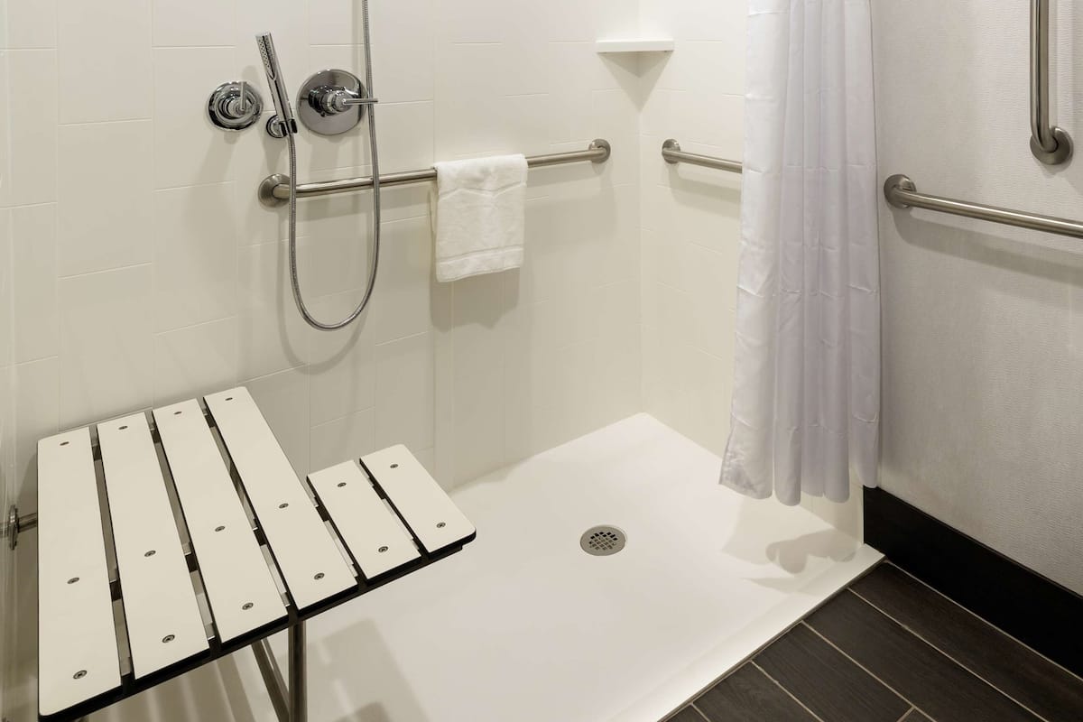 A modern shower area with a glass shower bench, grab bars, and a white curtain.