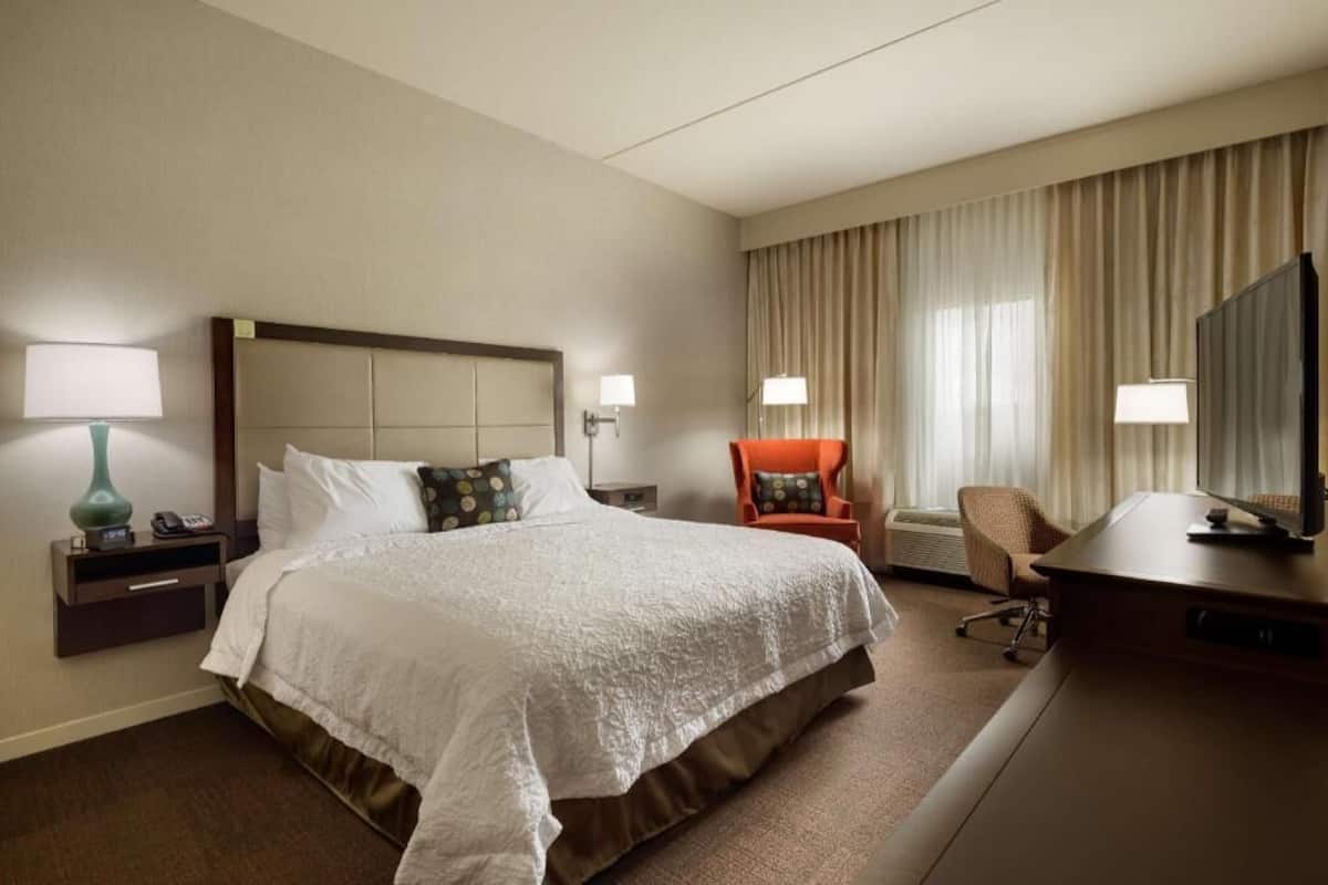 A hotel room with a large bed, a desk, a chair, a television, and a window with curtains.