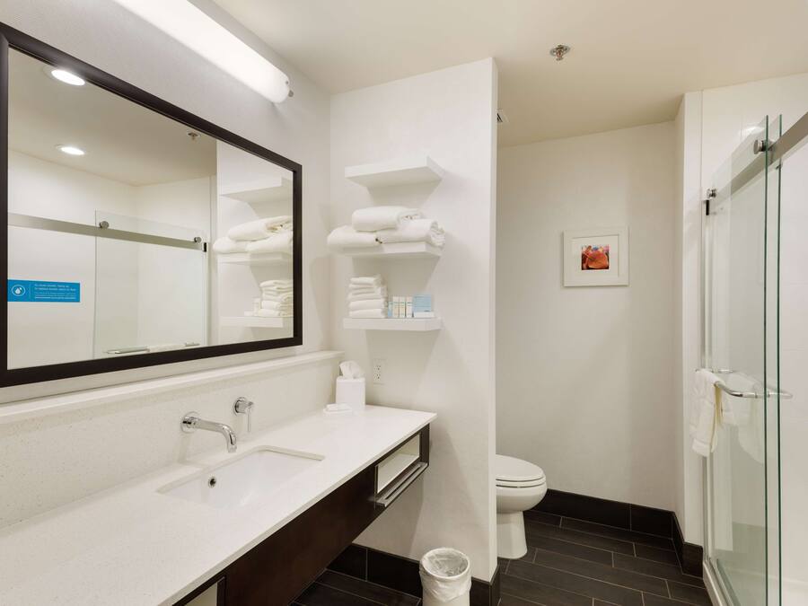 Un baño moderno con un espejo grande, un lavabo blanco y una cabina de ducha de vidrio.