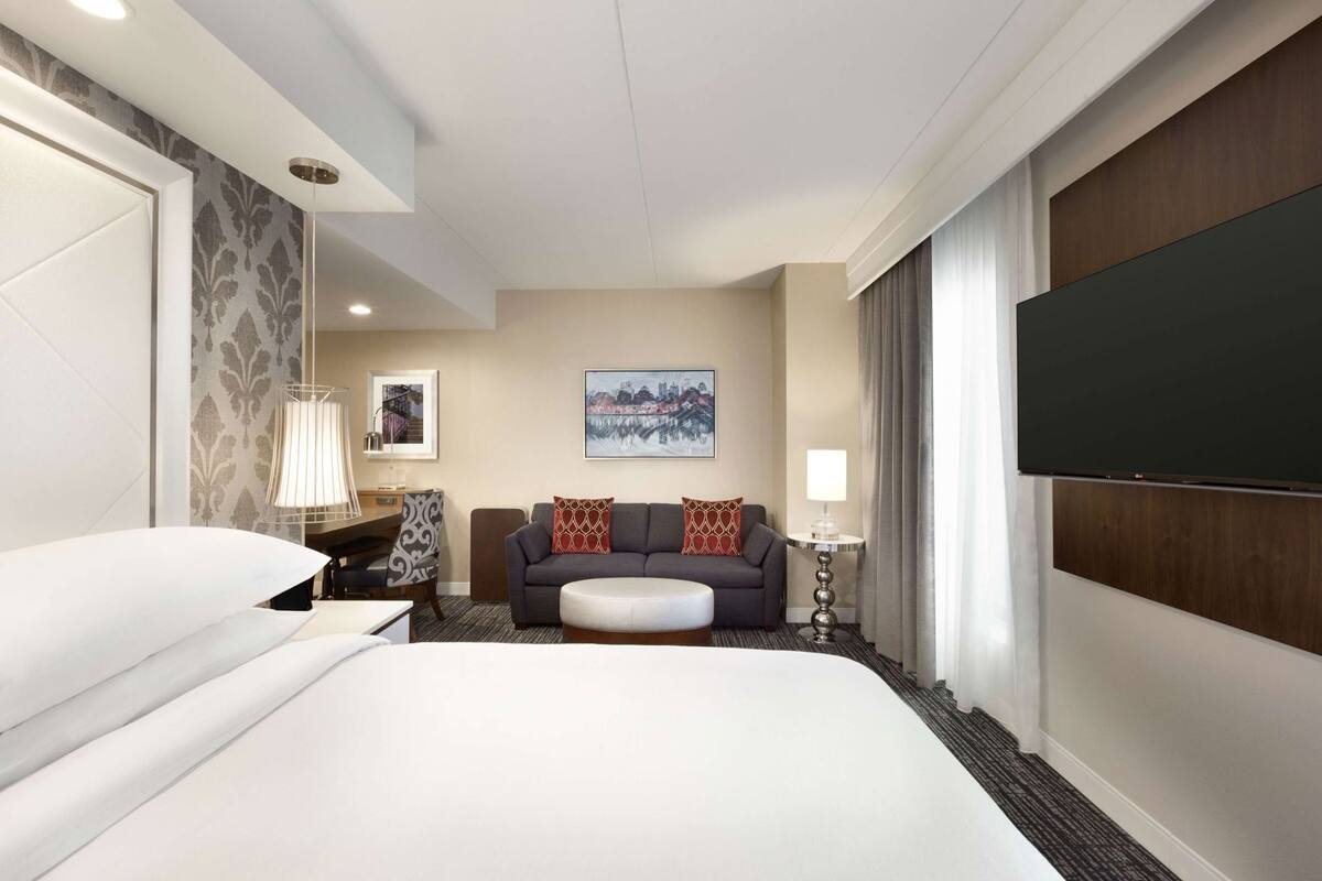 Une chambre d’hôtel avec un grand lit, un canapé, un bureau avec une lampe, une télévision et un tableau au mur.