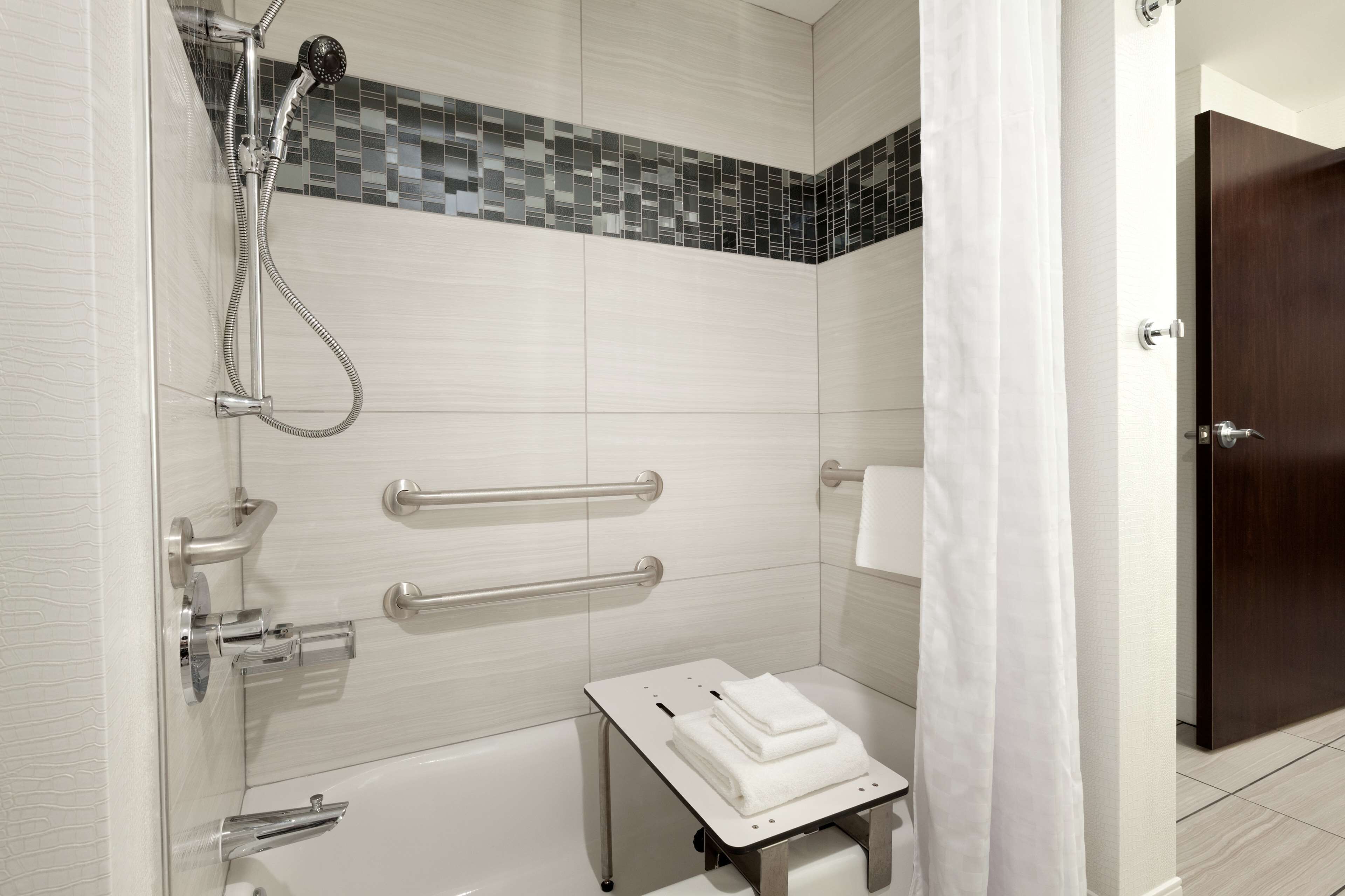 Un baño moderno con ducha, barras de apoyo, un lavamanos pequeño y un perchero para toallas.