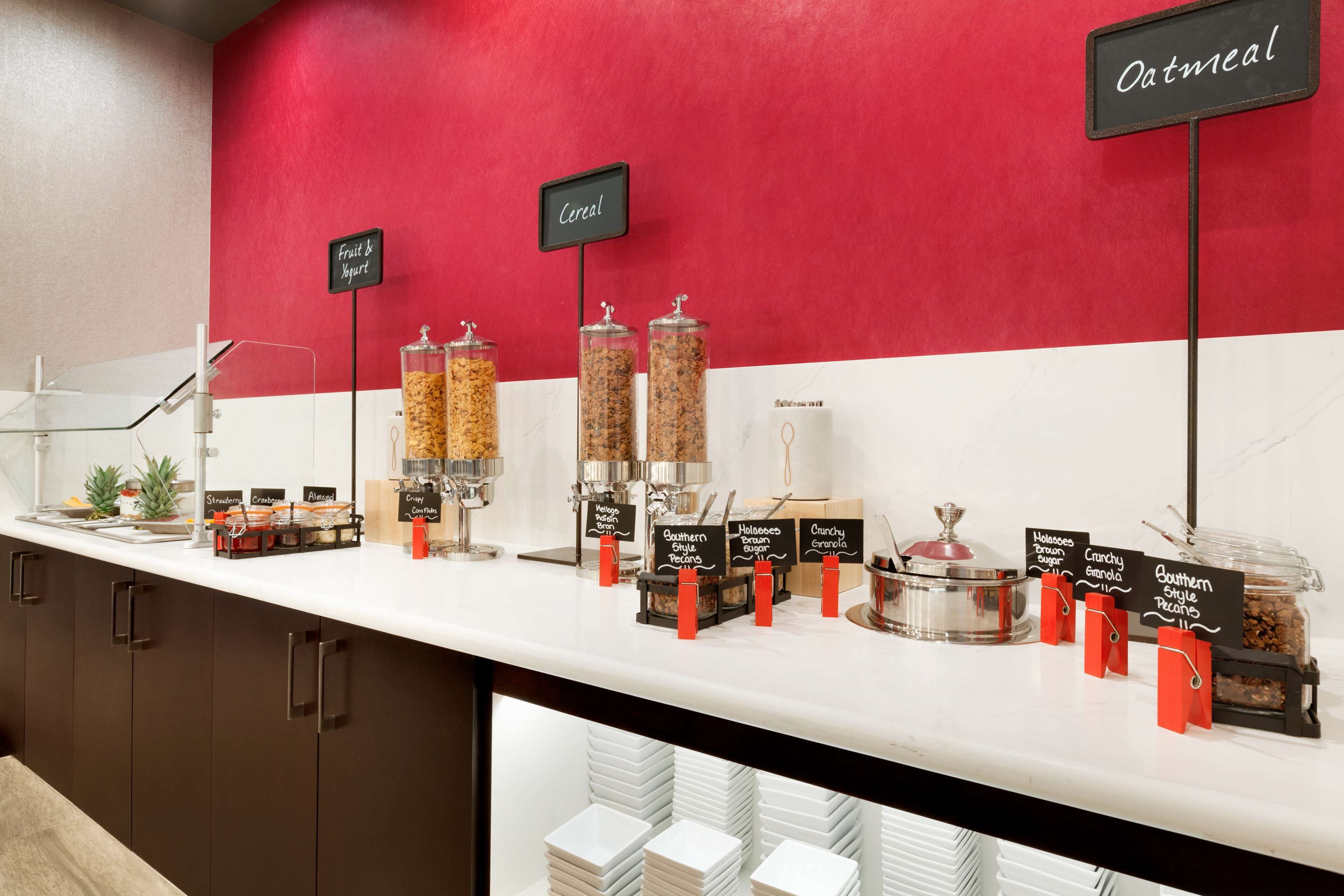 A breakfast bar with labeled dispensers for cereal, yogurt, and oatmeal.