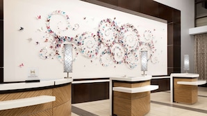 Un moderno vestíbulo de hotel con una gran instalación artística en la pared, varias recepciones y un diseño contemporáneo y limpio.