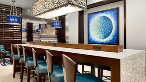 Un área de bar moderna con una barra larga, sillas azules e iluminación decorativa.