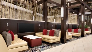 Un espacio lounge moderno con sofás y un televisor de pantalla plana, que presenta una pared con diseño y una alfombra azul.