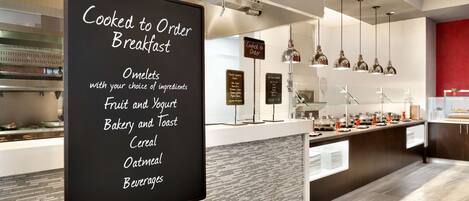 Zona de desayuno tipo buffet con cartel que muestra opciones de tortillas, fruta y yogur, panadería y tostadas, cereales, avena y bebidas.