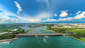 An aerial view of a coastal city with a prominent bridge over water, green areas, and a clear sky.
